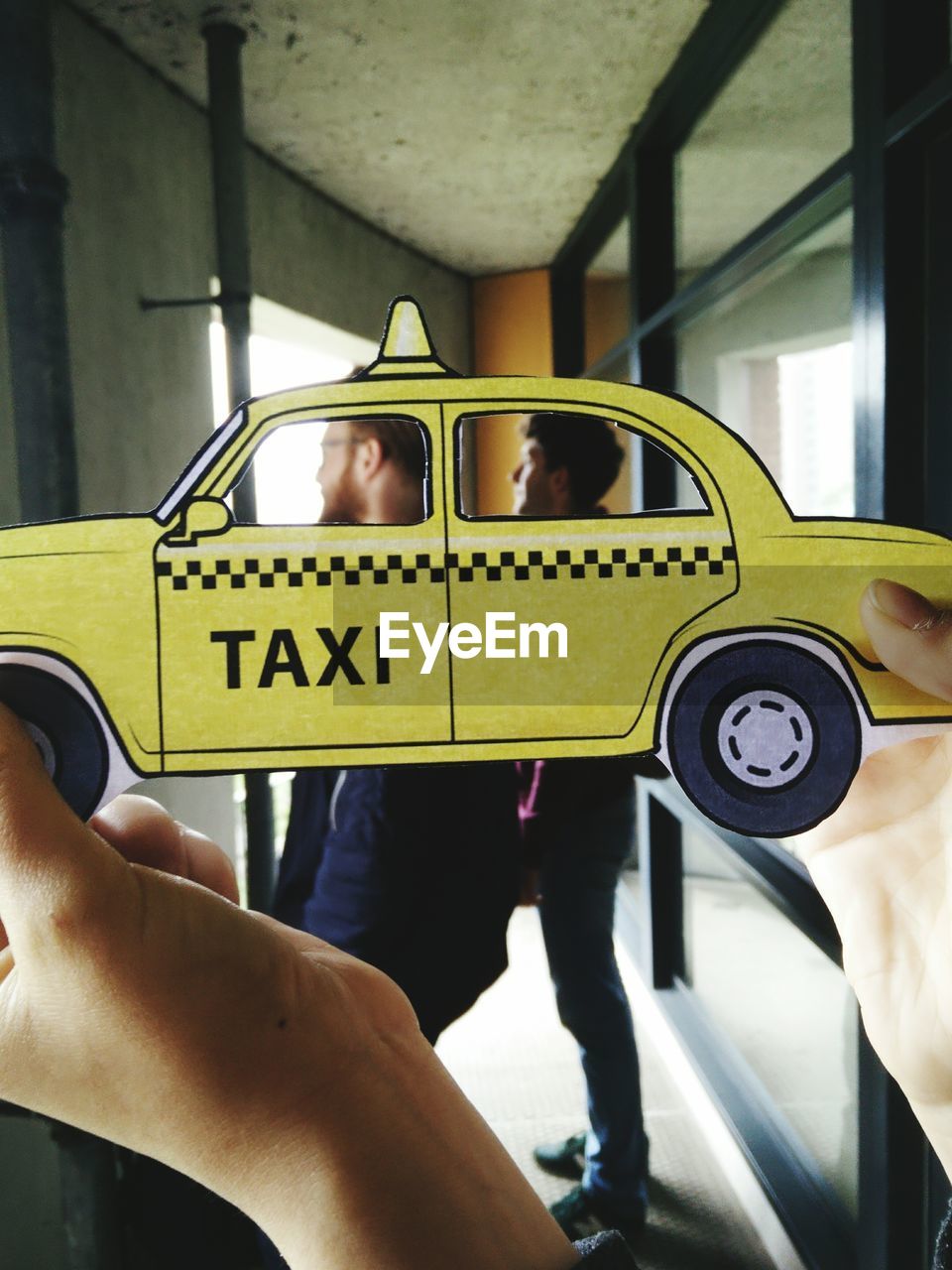 Cropped hand of man holding yellow taxi paper art against friends