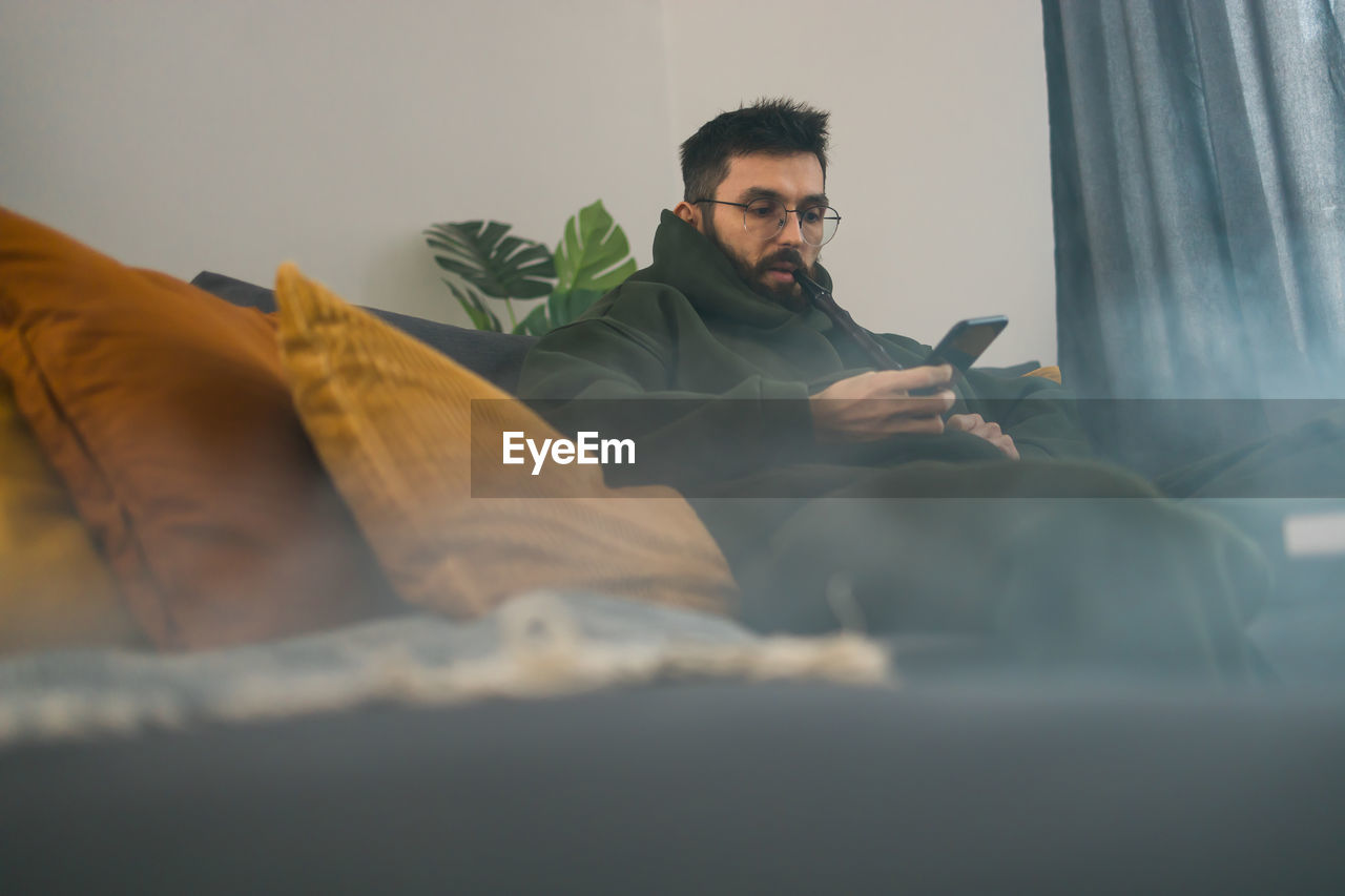 young man using mobile phone while lying on bed at home