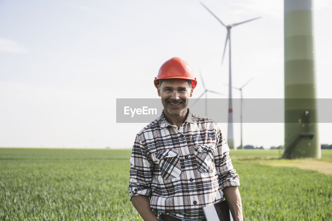 Smiling engineer wearing hardhat standing with tablet pc at field
