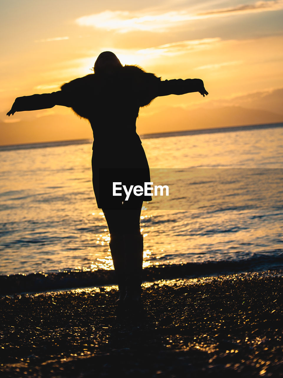 Silhouette woman with arms outstretched standing at beach during sunset