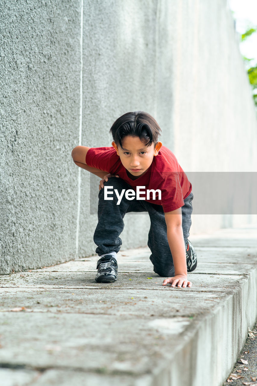 Full length portrait of boy kneeling on footpath