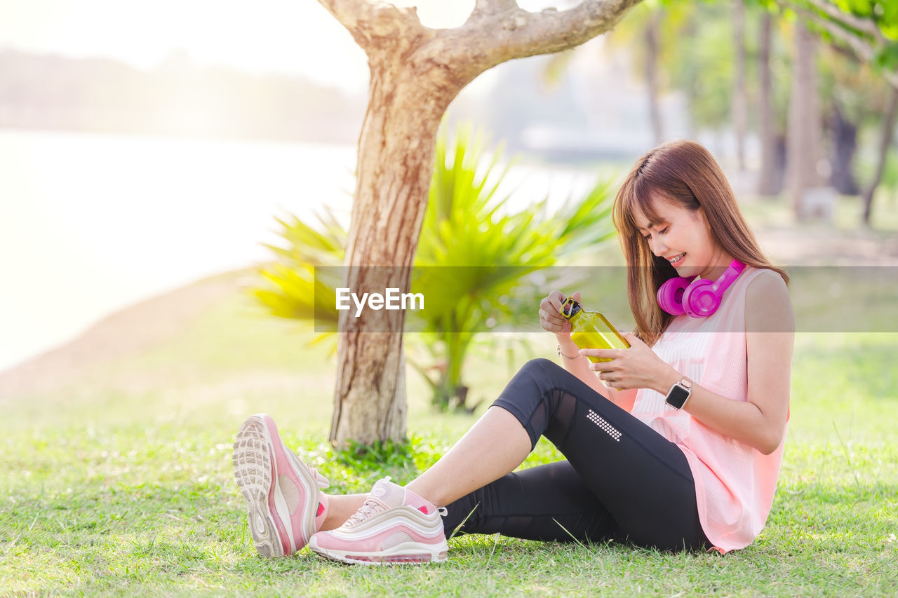 Young woman holding water bottle while sitting on grass