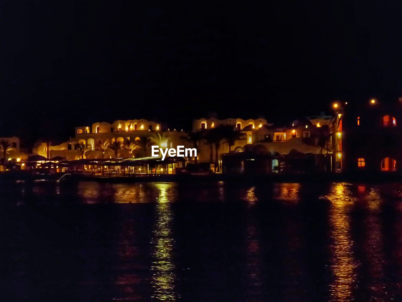 ILLUMINATED CITYSCAPE BY RIVER AGAINST SKY