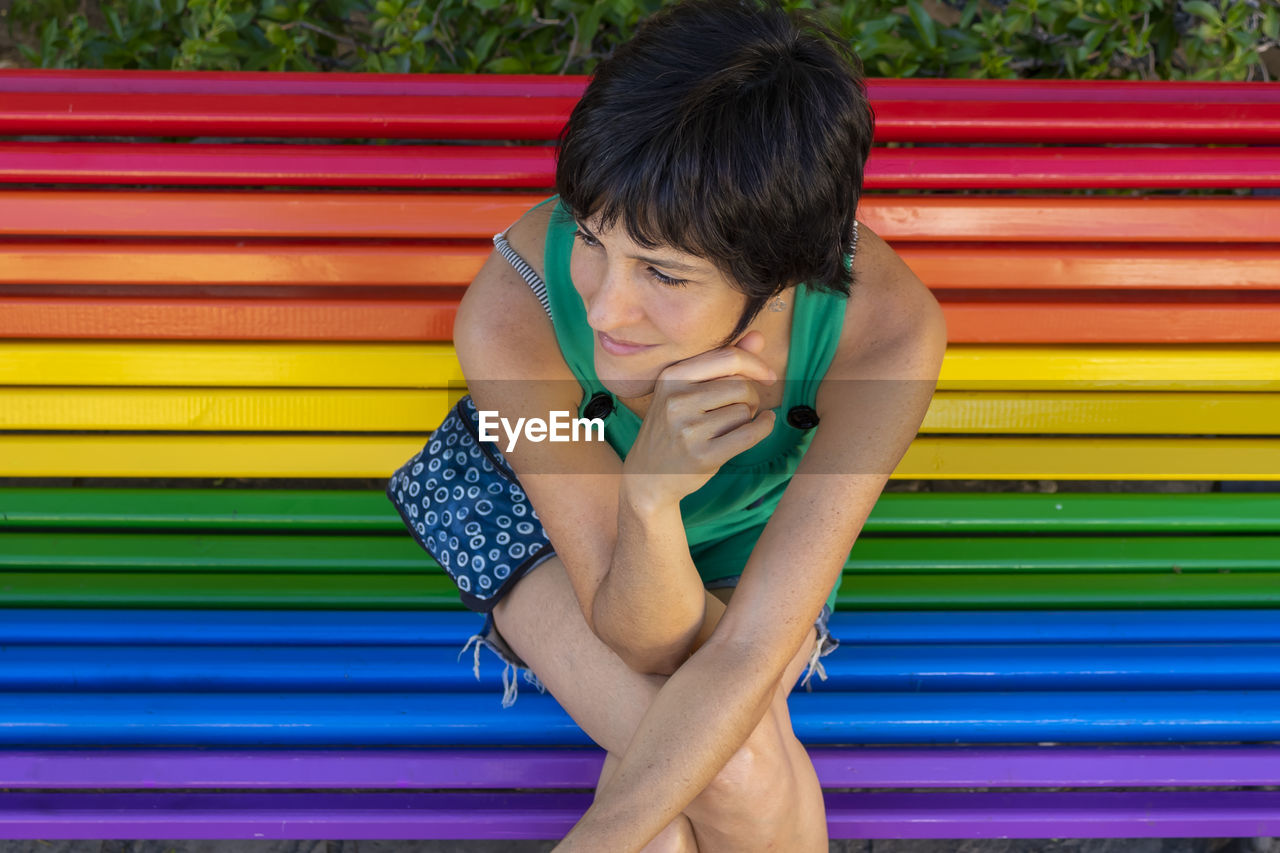 YOUNG WOMAN SITTING ON MULTI COLORED BENCH