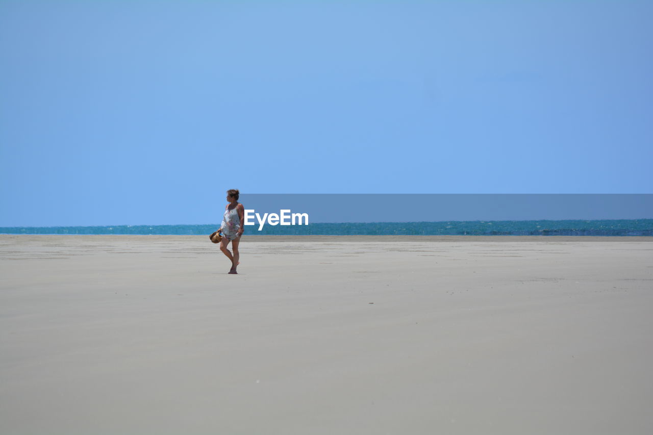 WOMAN ON BEACH AGAINST CLEAR SKY