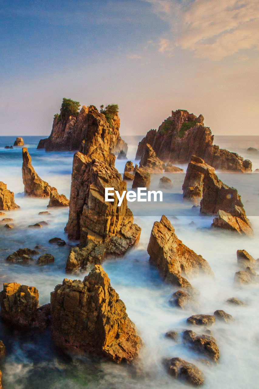 Rocks on beach against sky during sunset