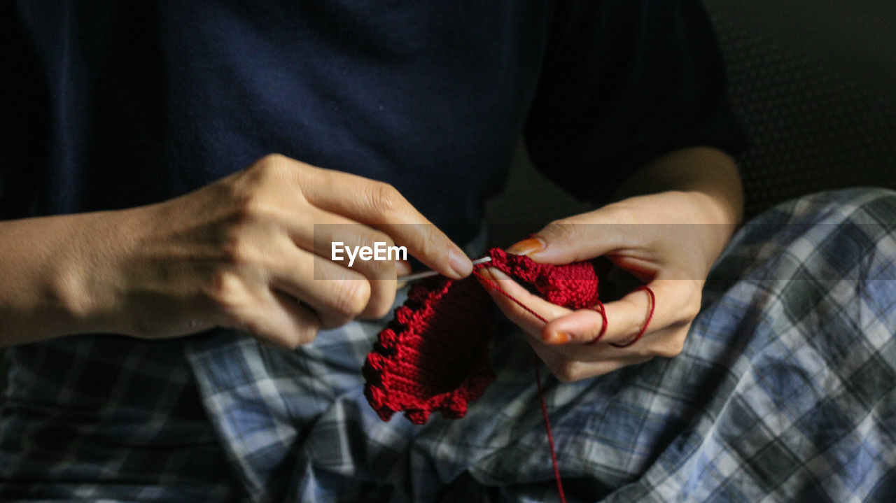 Midsection of person knitting red wool