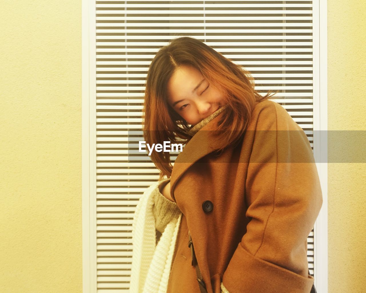 Portrait of young woman wearing jacket standing against wall