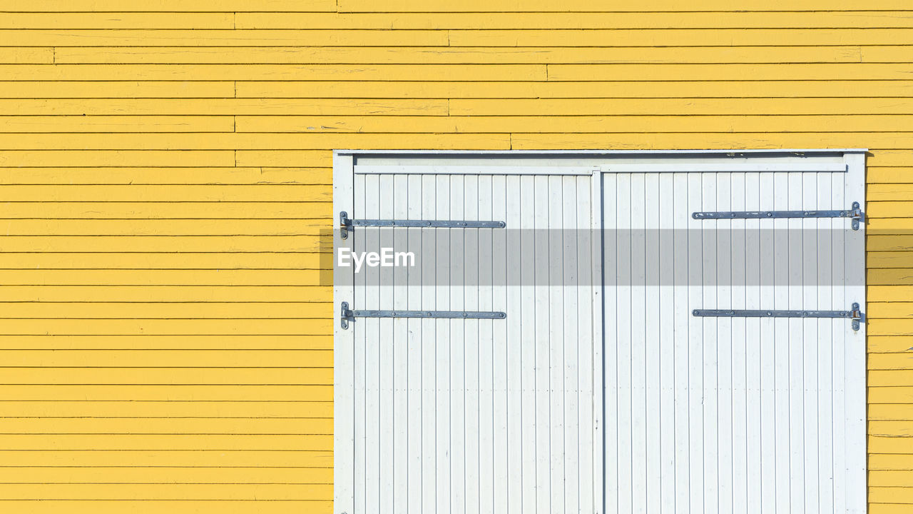 yellow, architecture, closed, built structure, door, wall - building feature, no people, pattern, shutter, building exterior, entrance, wood, backgrounds, striped, line, protection, building, full frame, textured, security, metal, window covering, day, white, copy space, outdoors