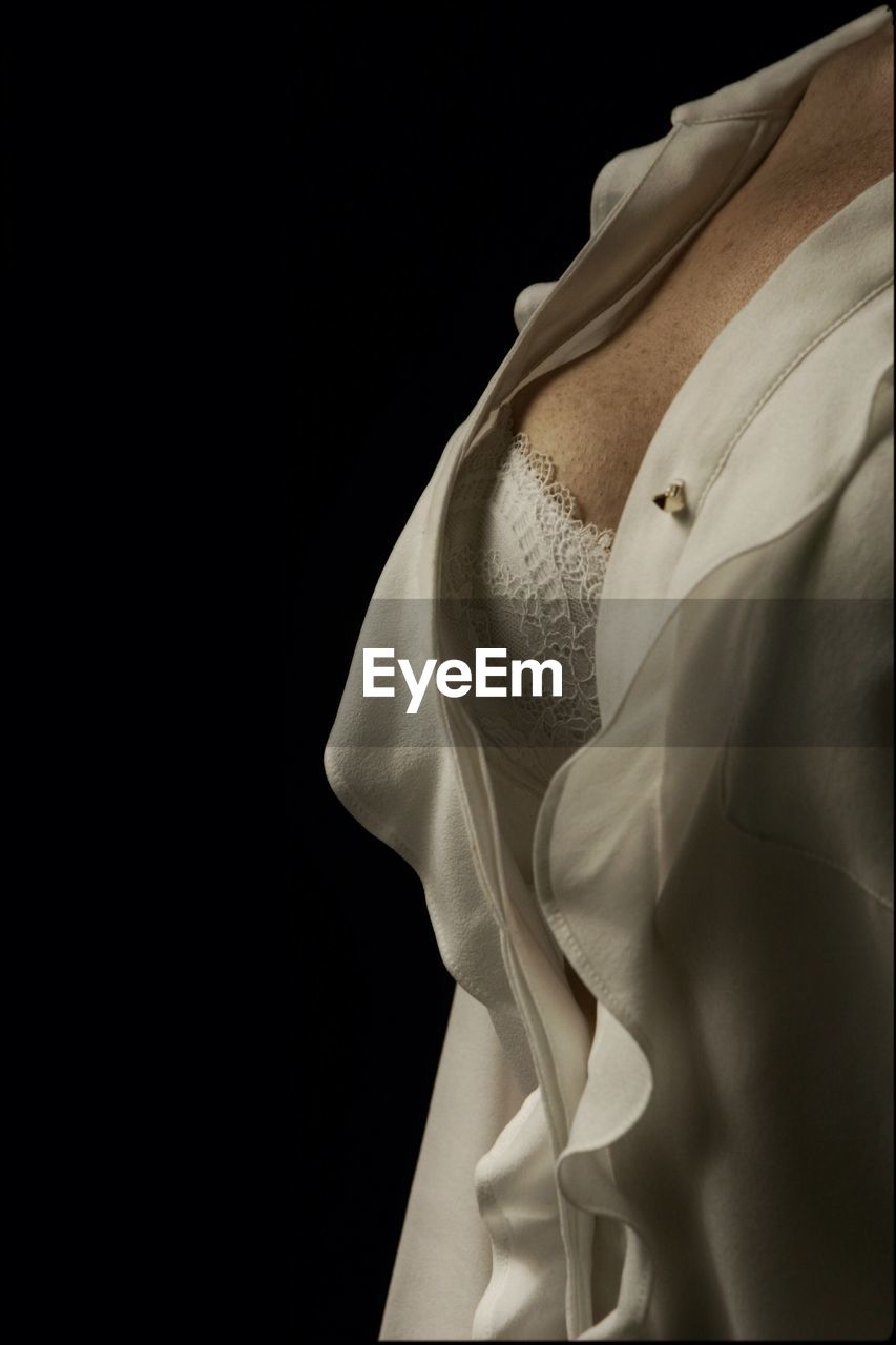 Close-up midsection of woman wearing white dress against black background