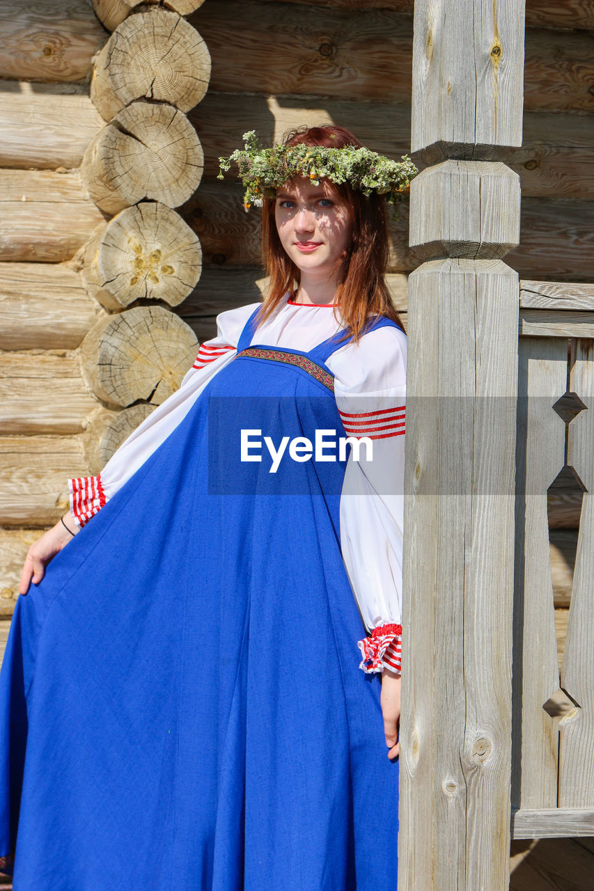 Portrait of young woman standing against wooden wall