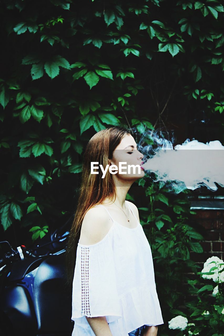 Woman exhaling smoke against trees