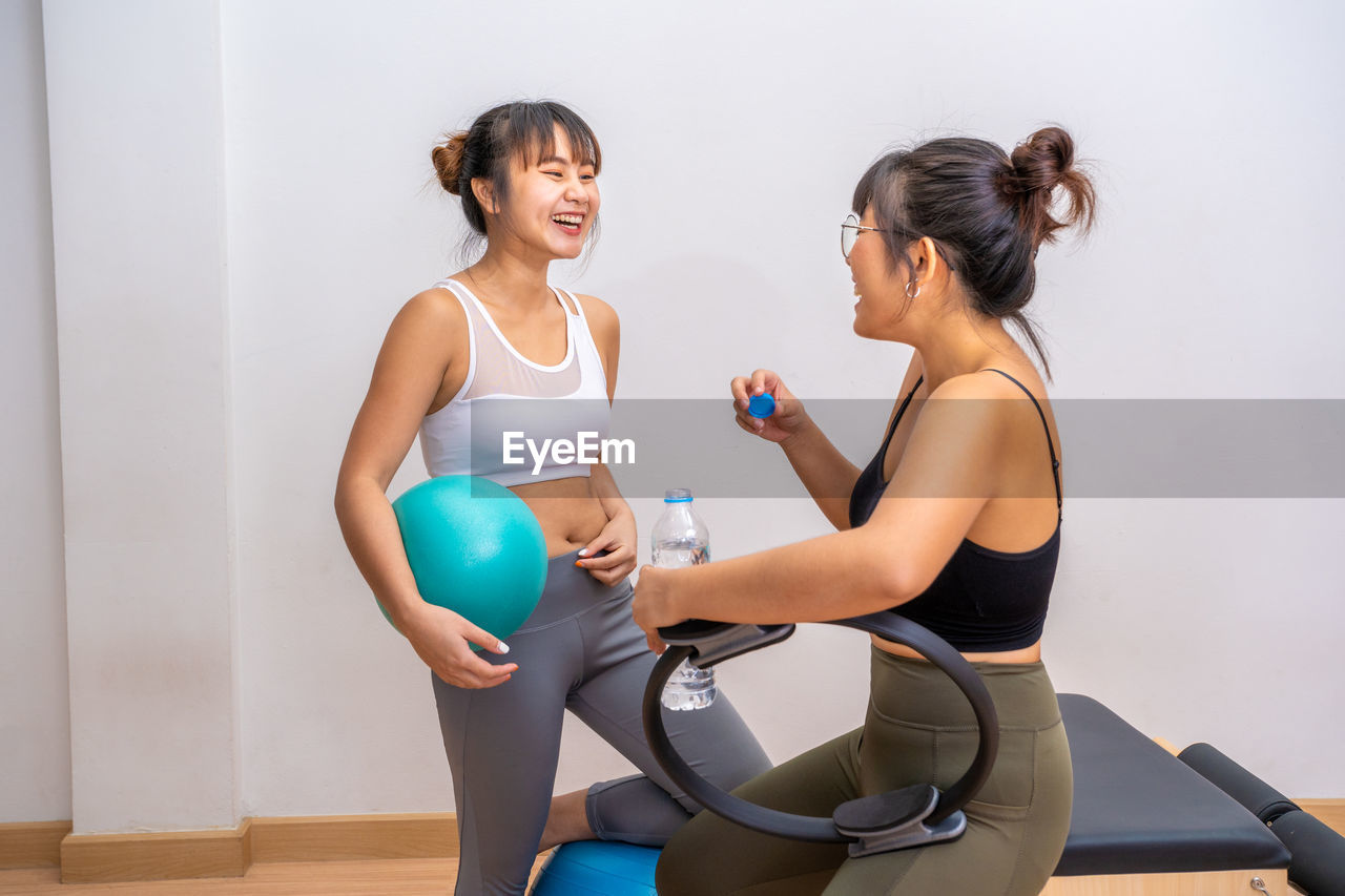 Two happy young asian women enjoy their conversation while taking break from their pilates exercise