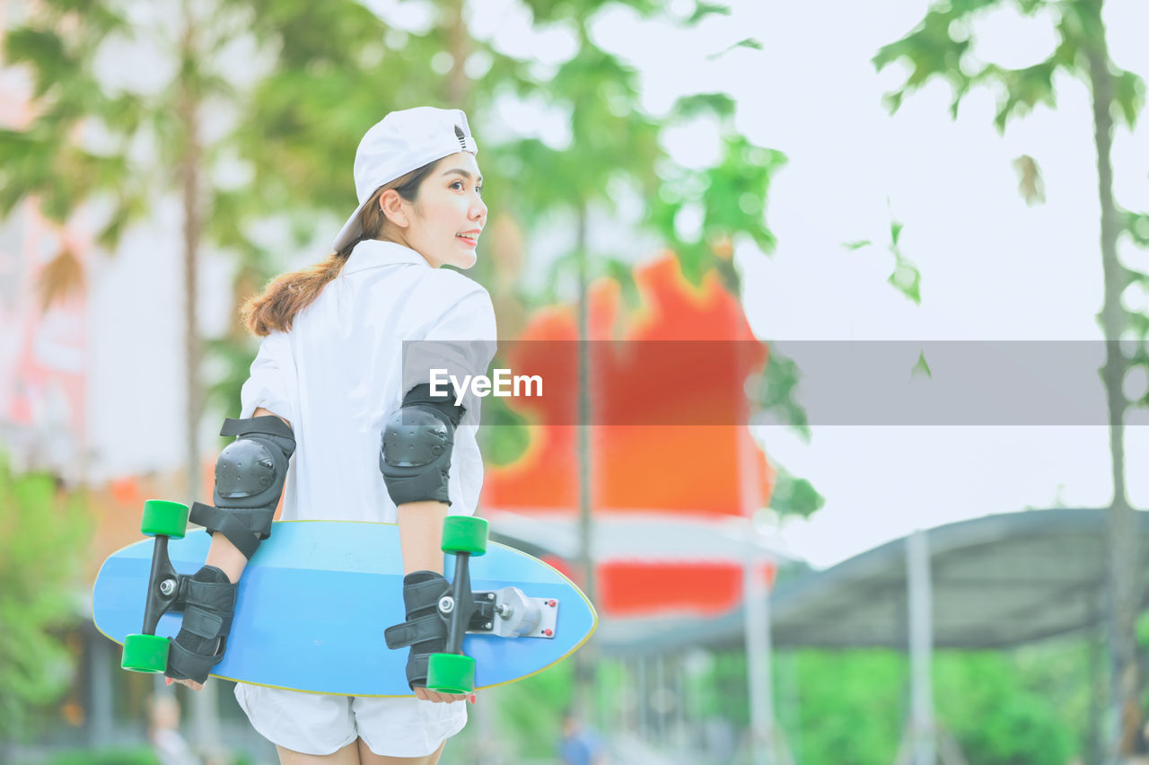 Woman holding skateboard while standing outdoors