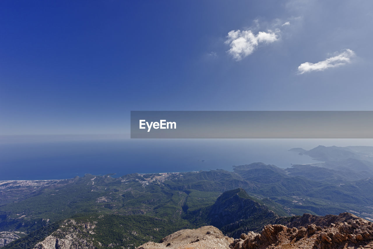 Aerial view of sea and mountains against blue sky