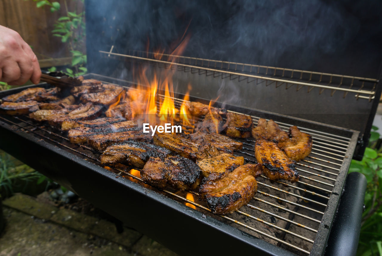 Cropped hand preparing meat on barbecue grill