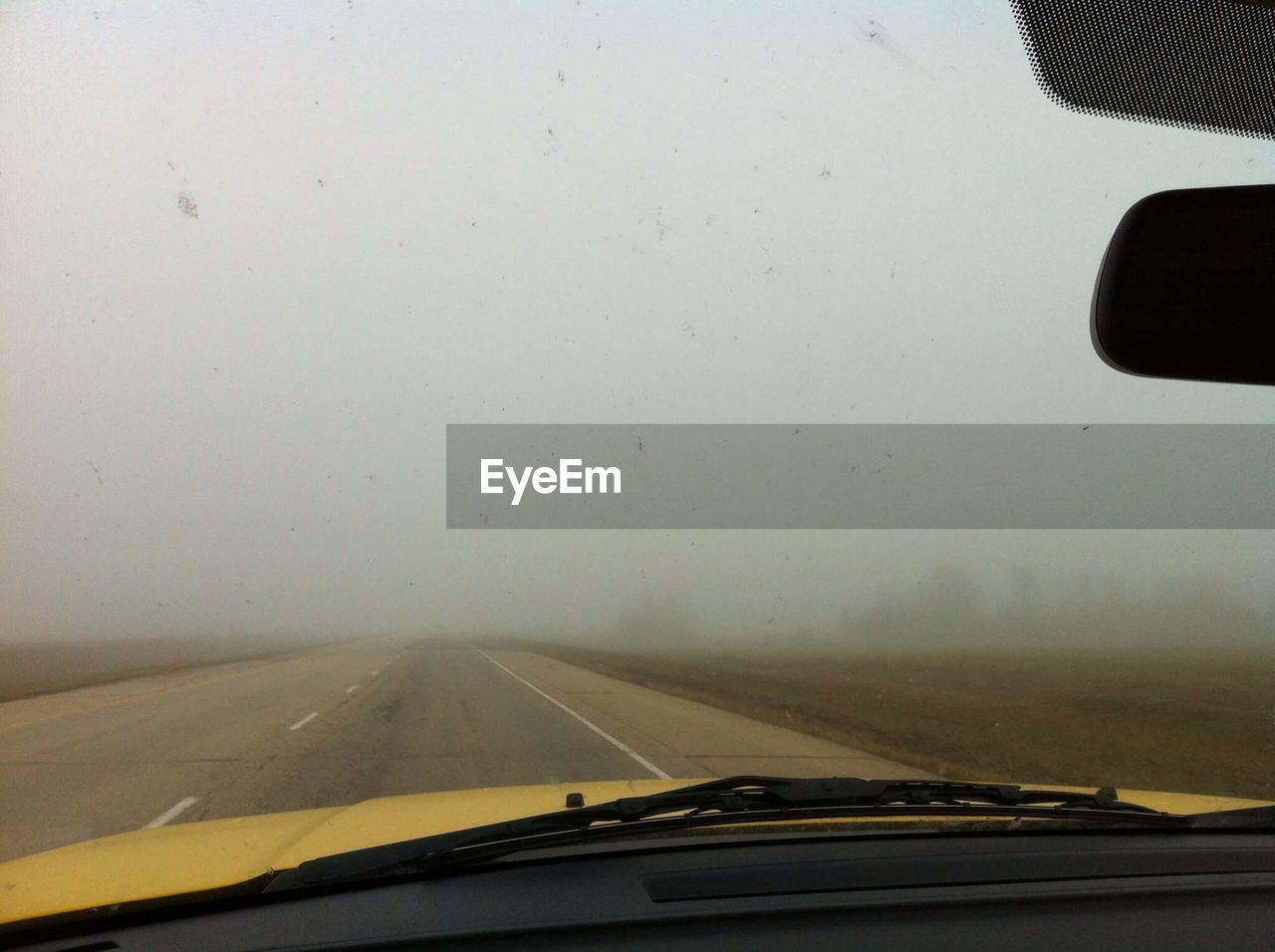 Country road against foggy weather seen from car windshield