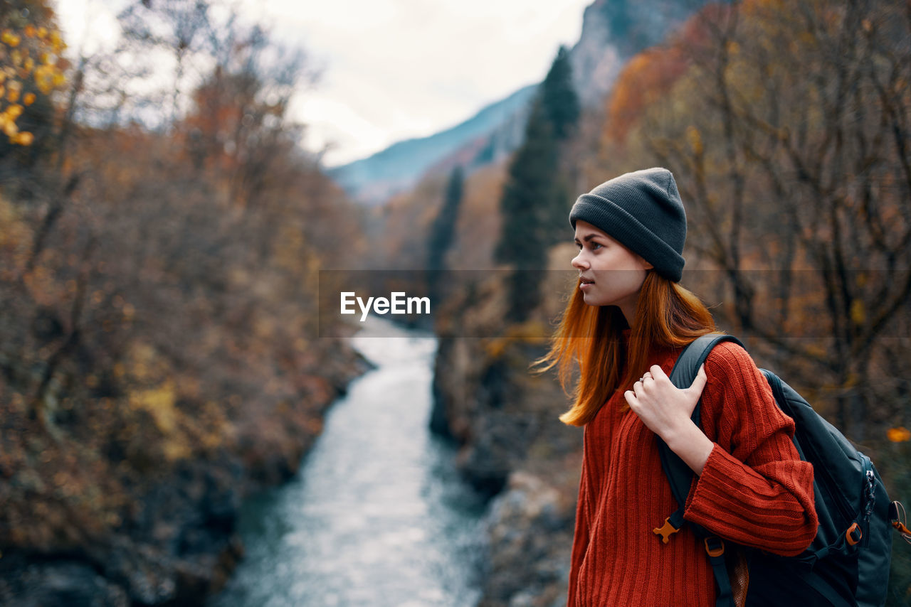 YOUNG WOMAN LOOKING AWAY WHILE STANDING IN PARK DURING WINTER