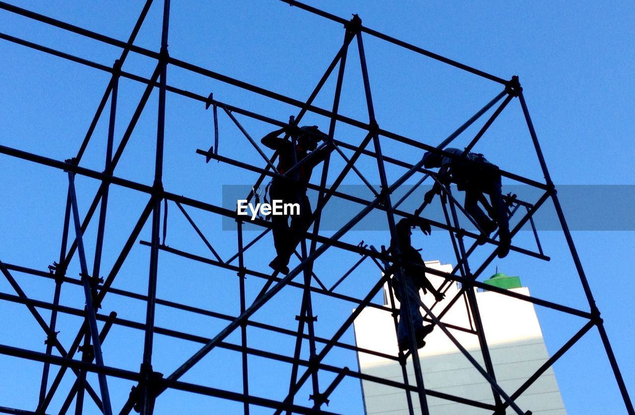 Low angle view of silhouette manual workers on scaffoldings against clear sky