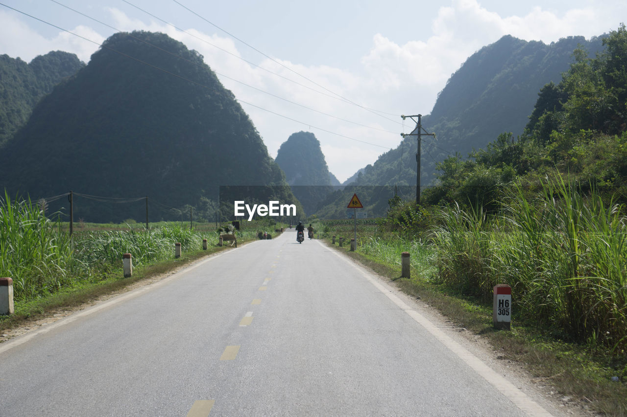 ROAD AMIDST TREES AGAINST MOUNTAINS