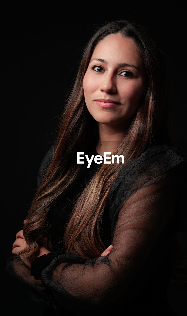 Portrait of smiling young woman against black background