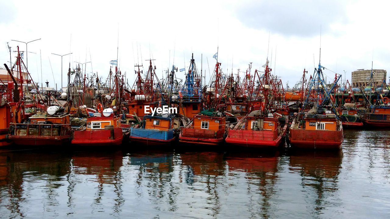 BOATS MOORED ON RIVER BY HARBOR AGAINST SKY