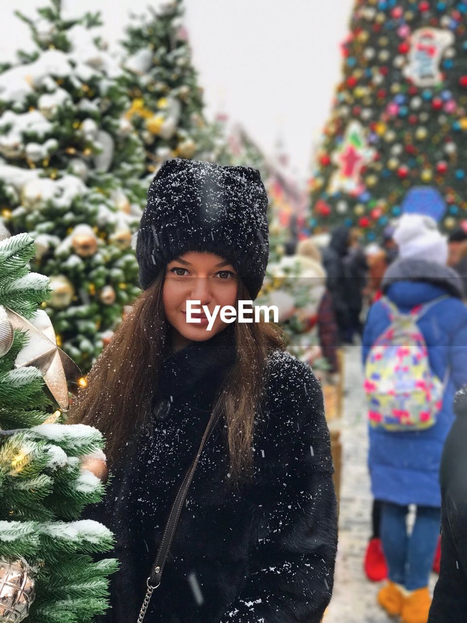 Portrait of young woman standing amidst christmas trees during winter