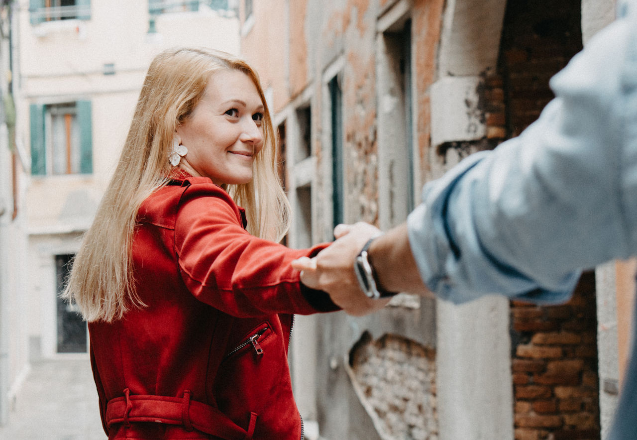 Young couple holding hands while standing against building in city