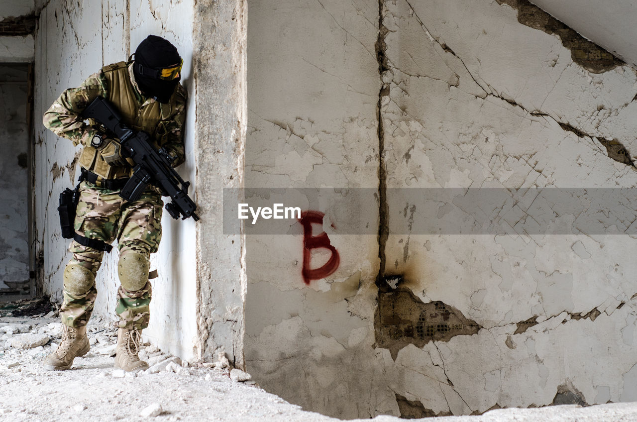 Man holding rifle while standing against wall