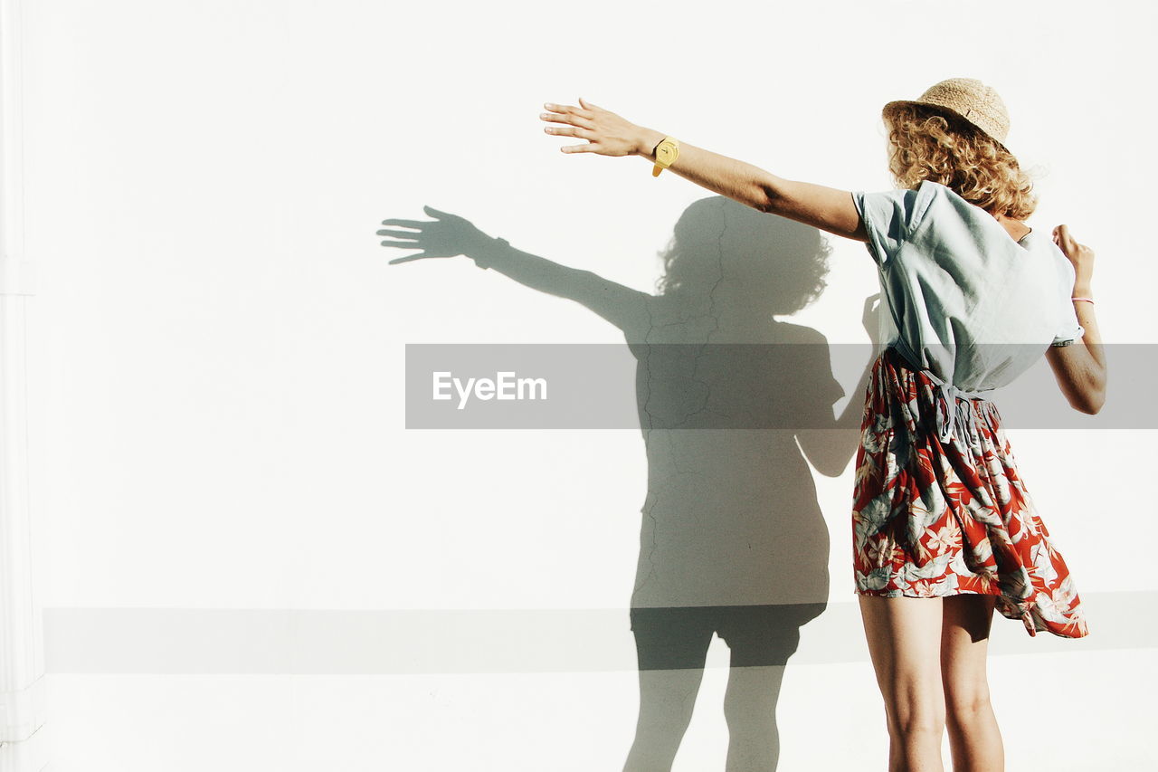 Rear view of woman standing with shadow on white wall