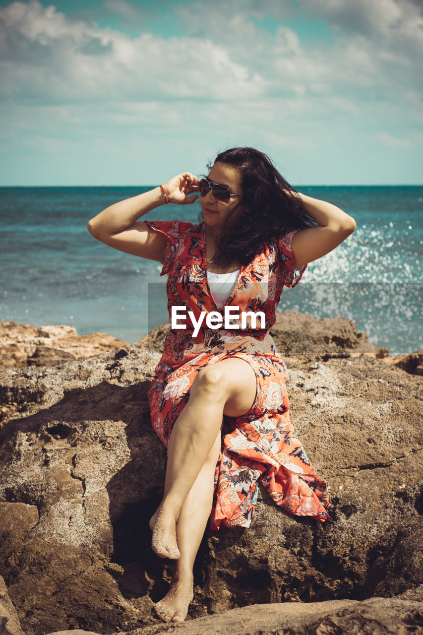 Full length of woman sitting on rock at beach