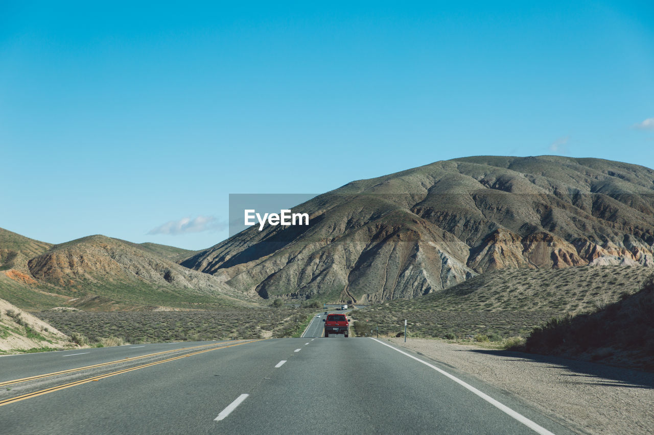 Vehicles on road by mountain against clear blue sky