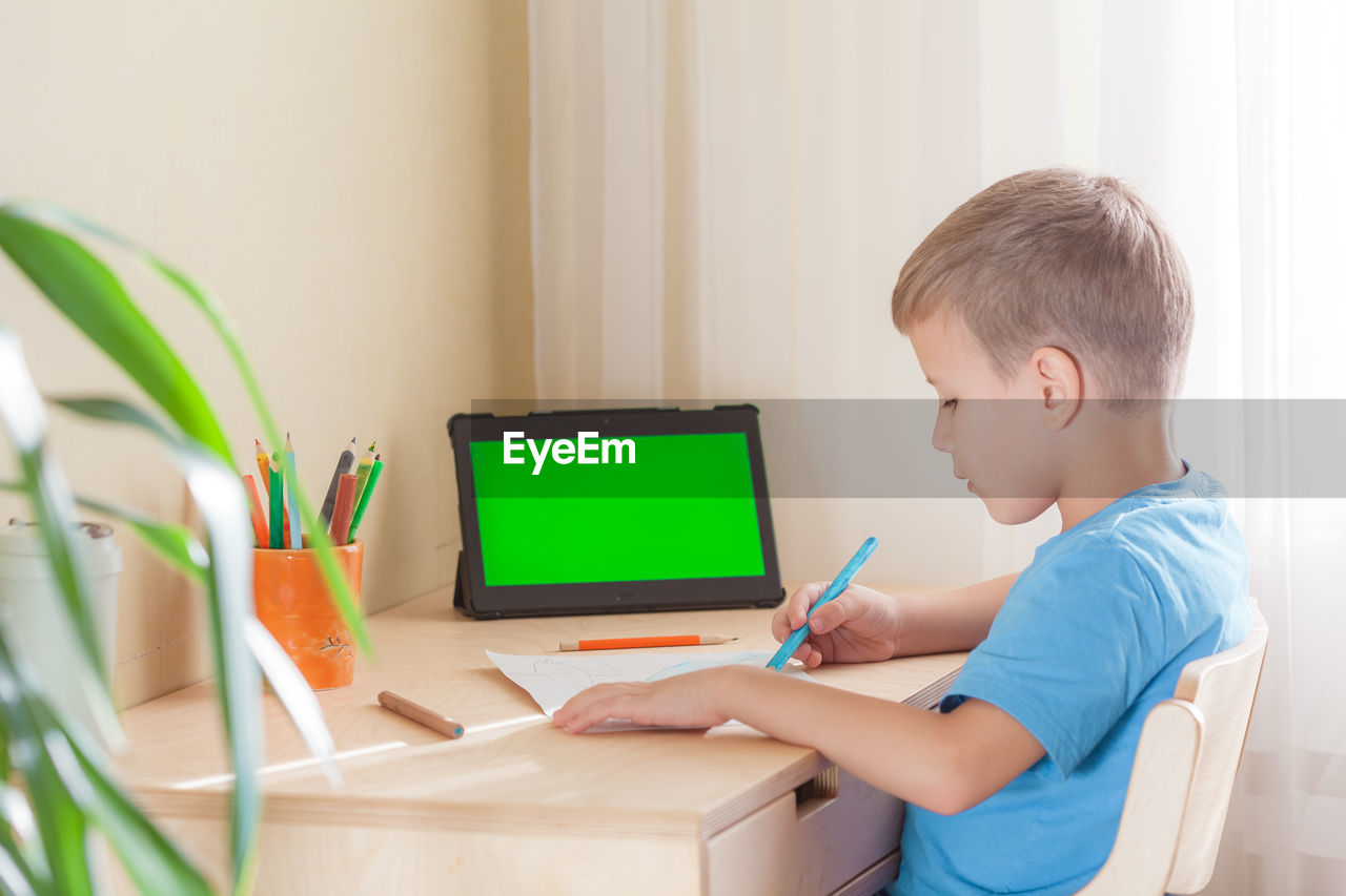 Smart school boy drawing picture, tablet with green screen stay on desk. distance learning concept.