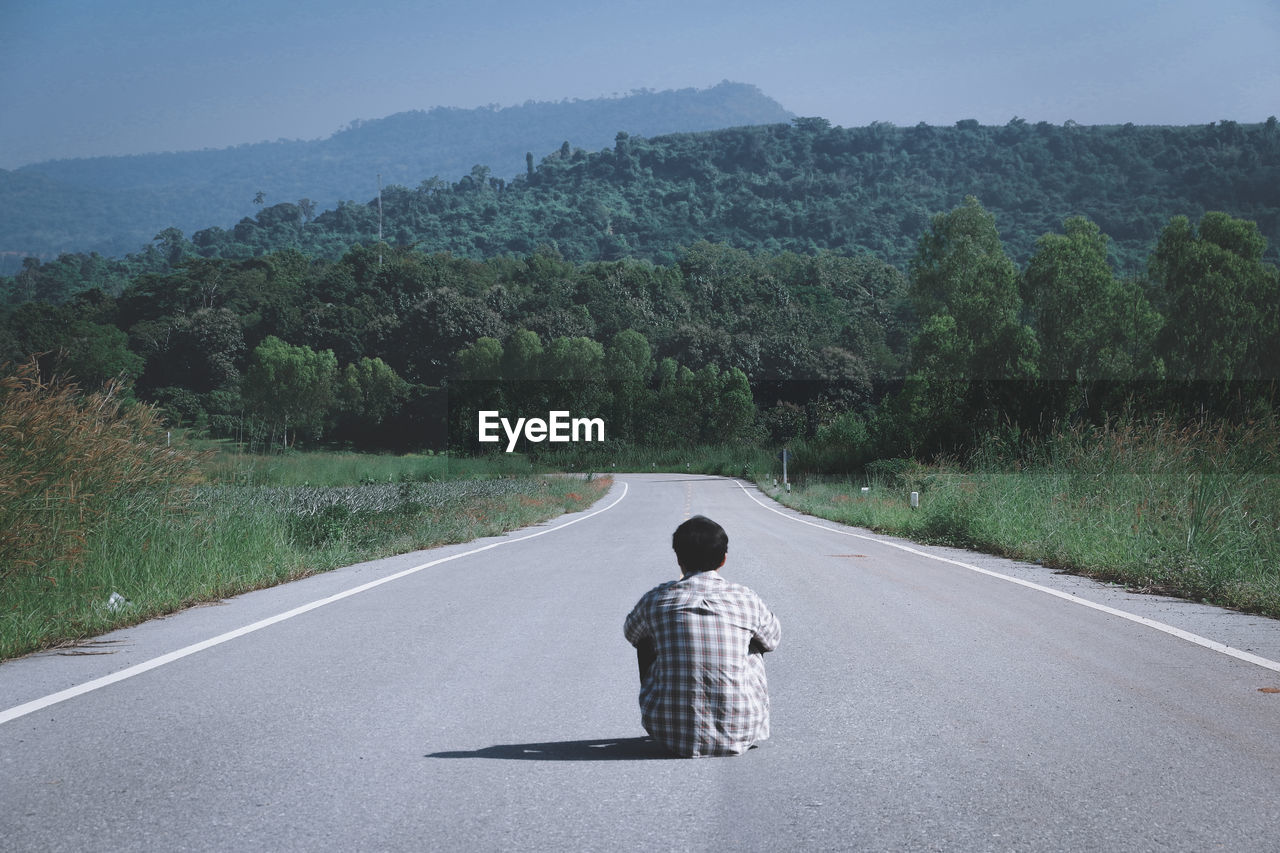 Rear view of man sitting on country road