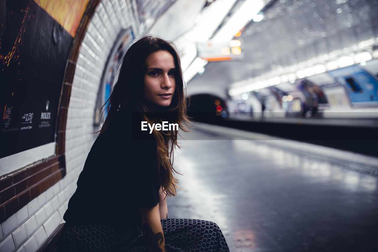 Side view portrait of young woman sitting at railroad station platform