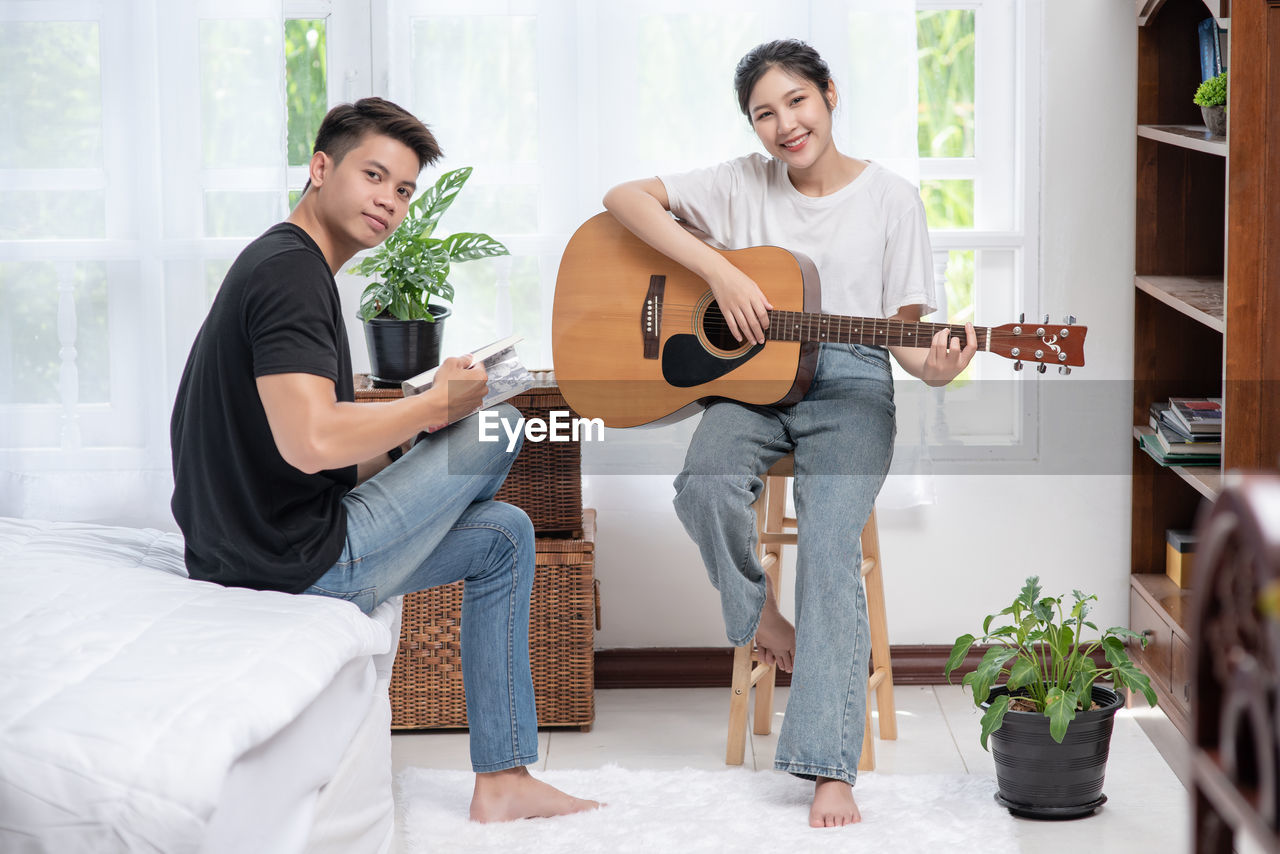 YOUNG COUPLE PLAYING GUITAR AT HOME