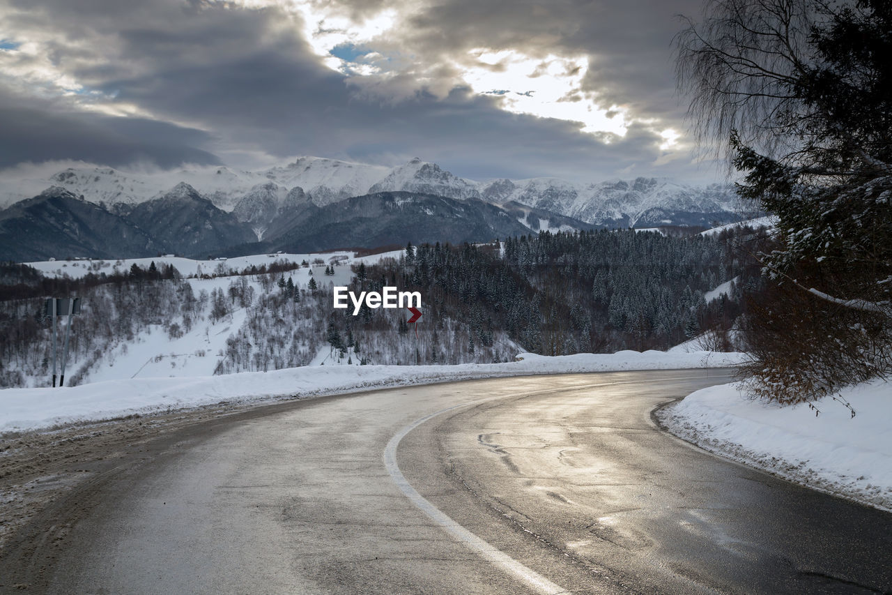 Road by mountains against sky during winter