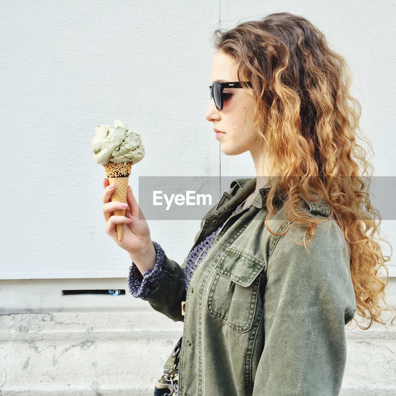 Young woman looking at ice cream while standing against wall