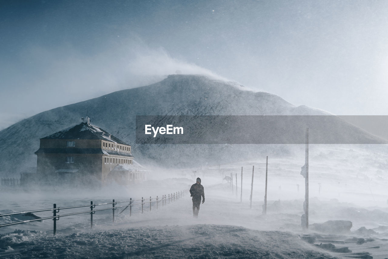 REAR VIEW OF PERSON STANDING ON SNOWCAPPED MOUNTAIN AGAINST SKY