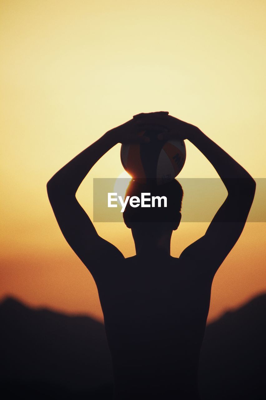 Silhouette man with volleyball against sky during sunset