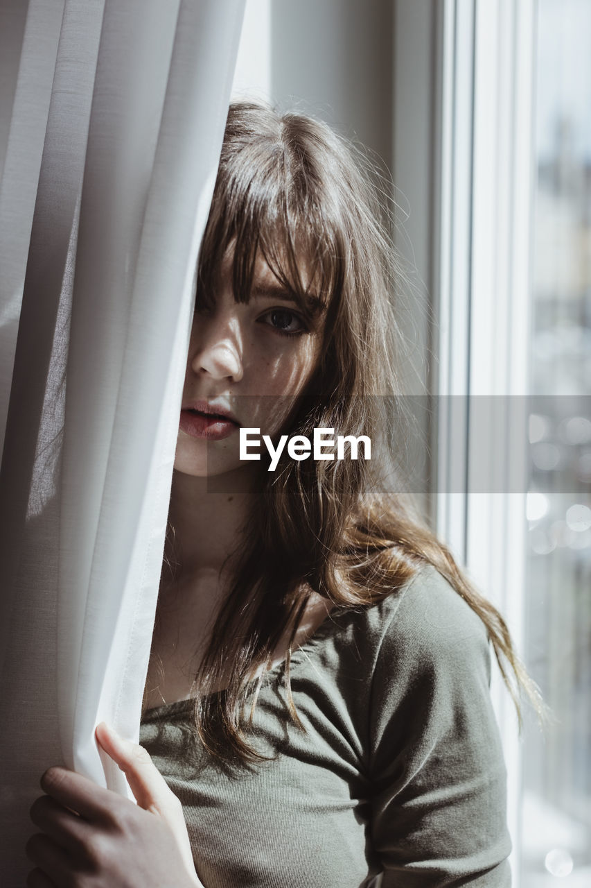 Portrait of woman standing by curtain