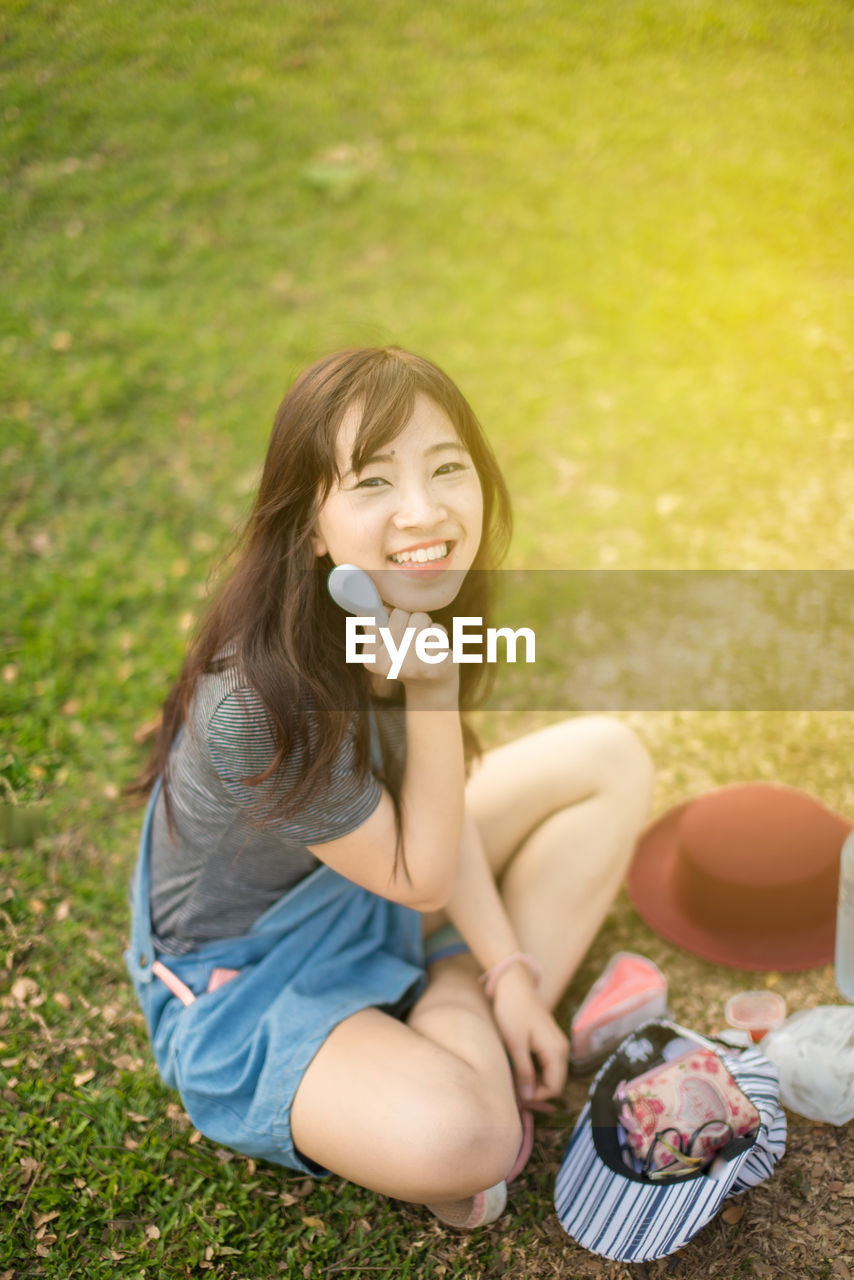 High angle portrait of young woman holding spoon while sitting on field at park