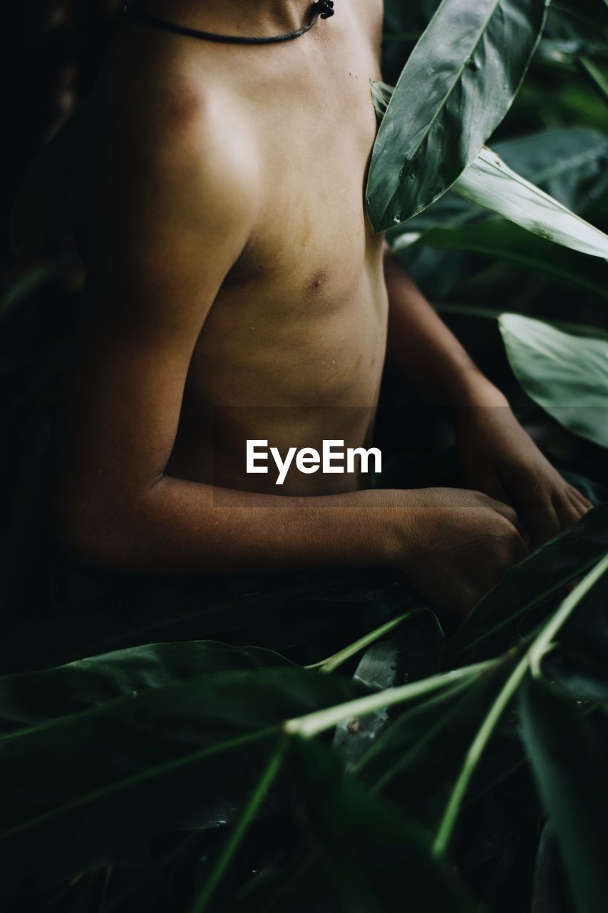 Close-up of shirtless man chopping leaves at forest