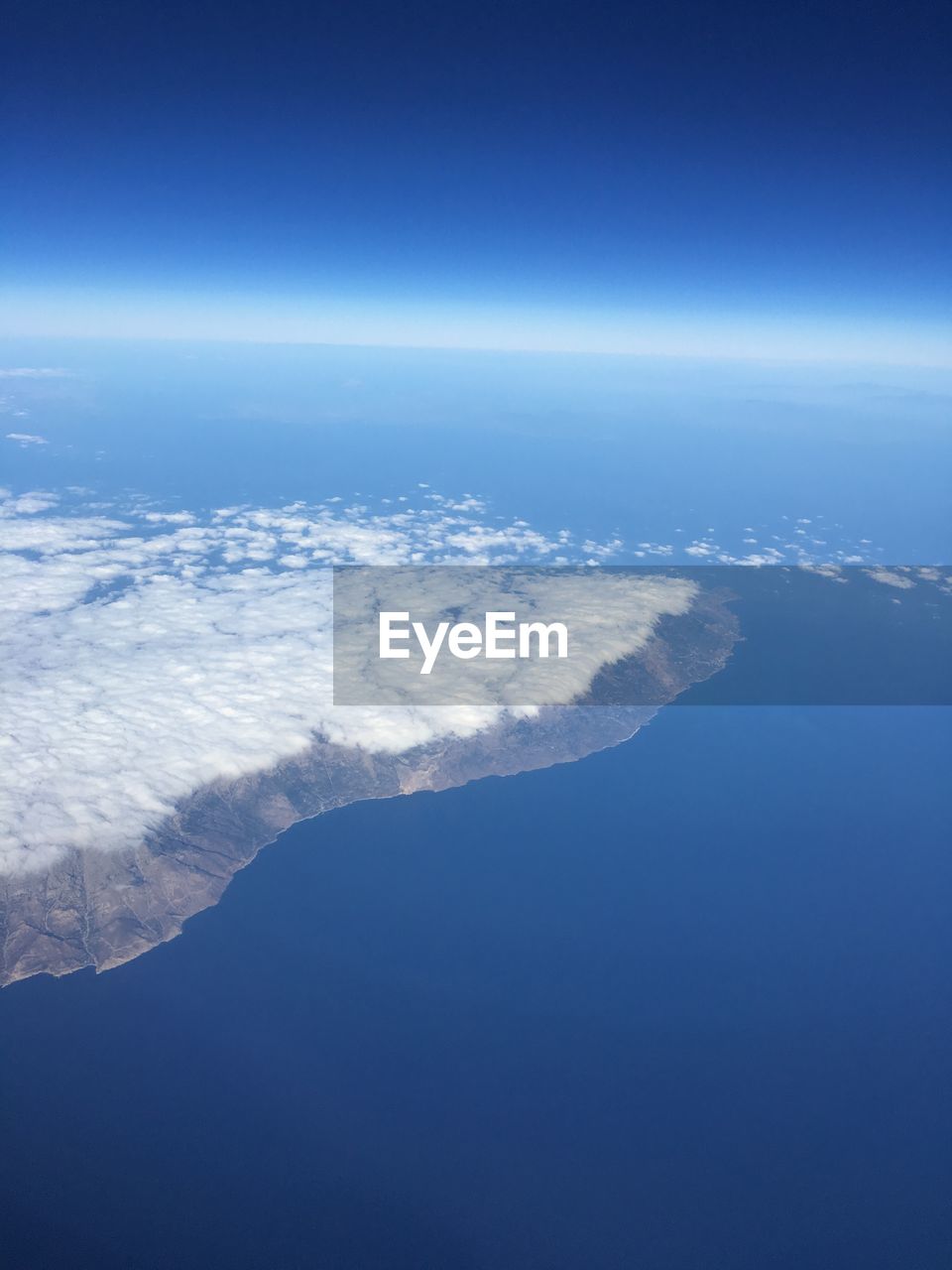 Aerial view of clouds over mountains by blue sea