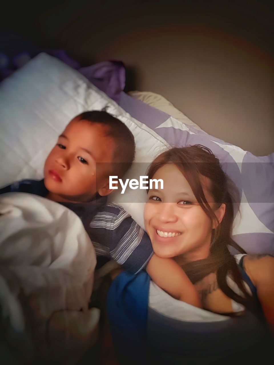 Son touching mother breast while lying on bed at home