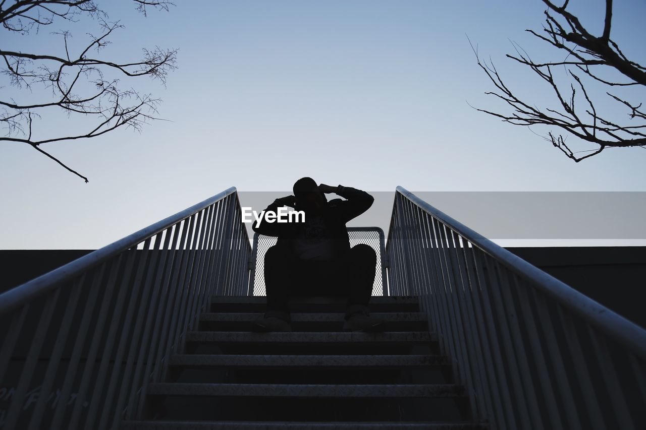 Low angle view of silhouette man sitting on steps against sky