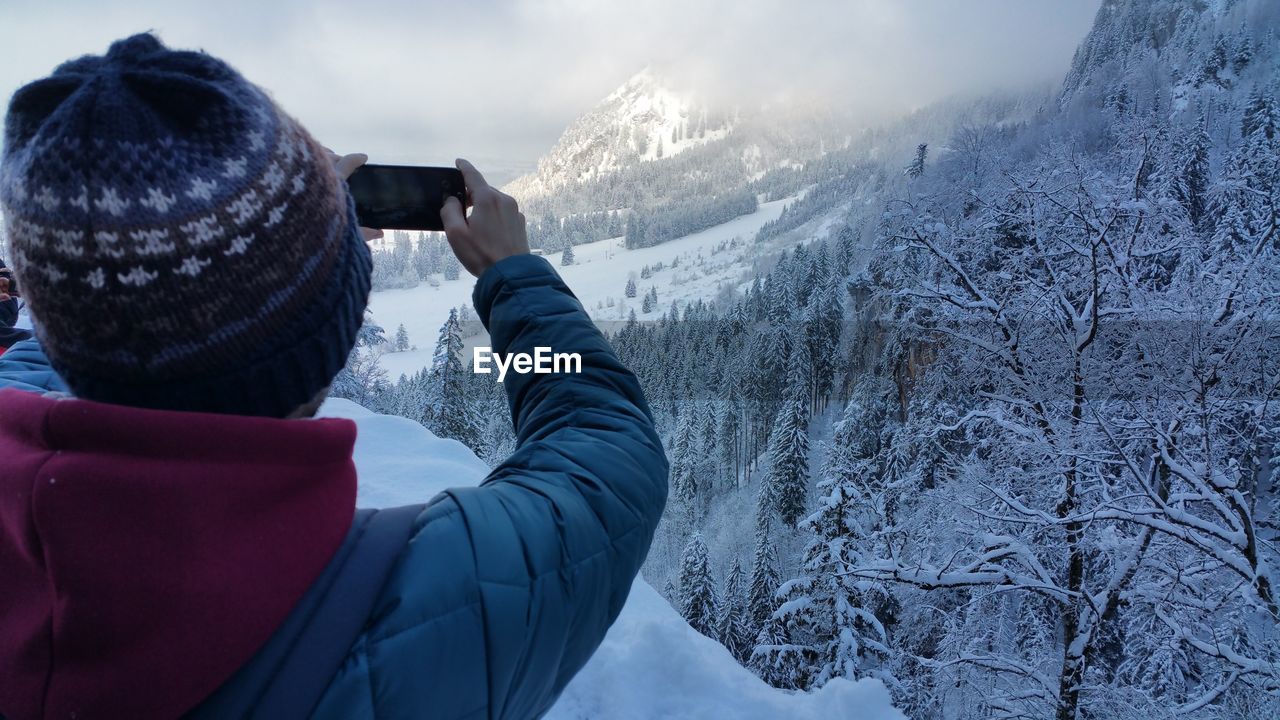 Rear view of man photographing mountains during winter using smart phone
