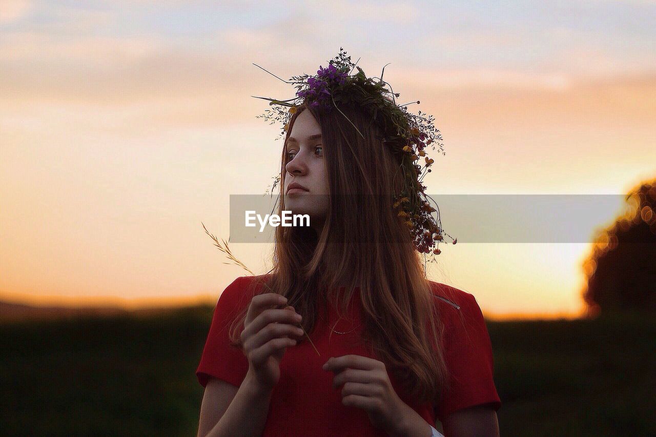 Woman wearing flowers against sky during sunset