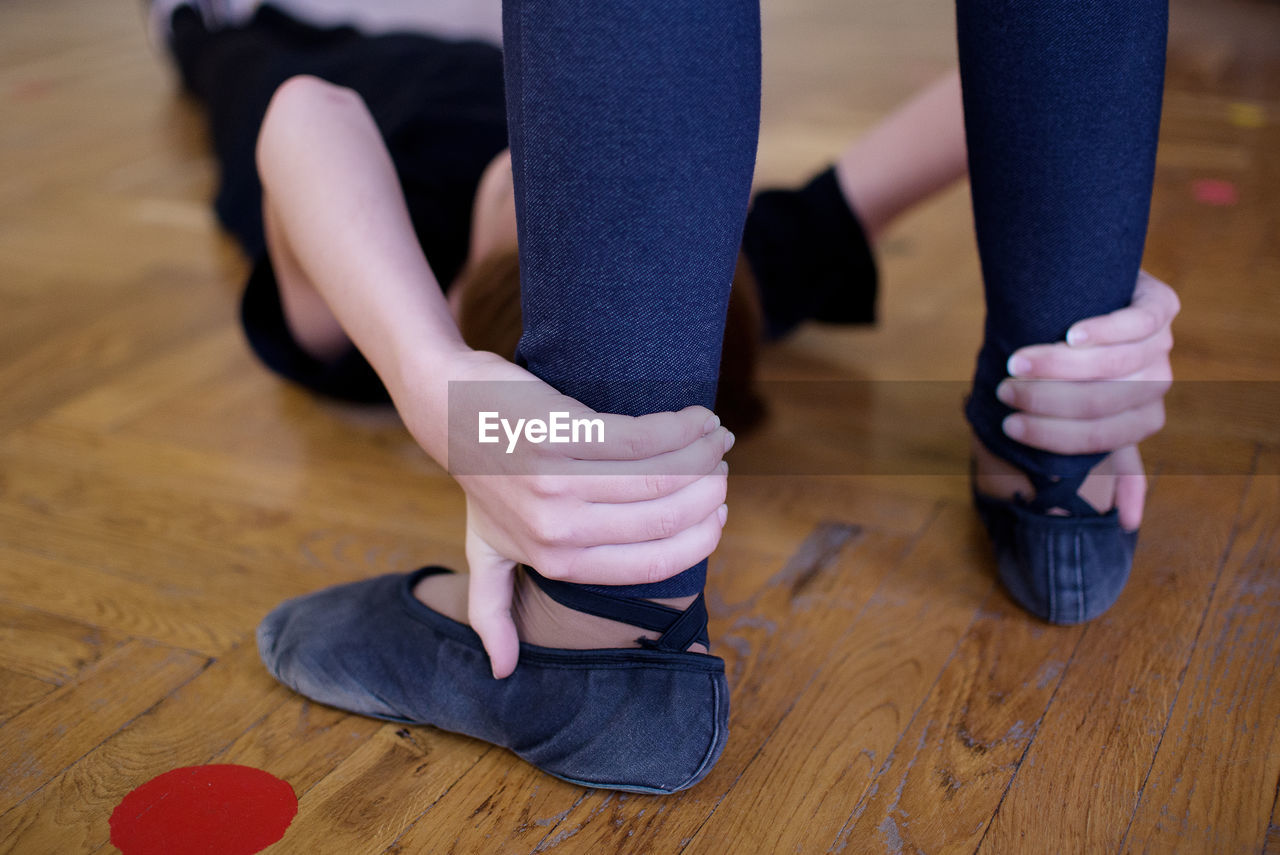 Low section of woman holding legs of friend while lying on hardwood floor