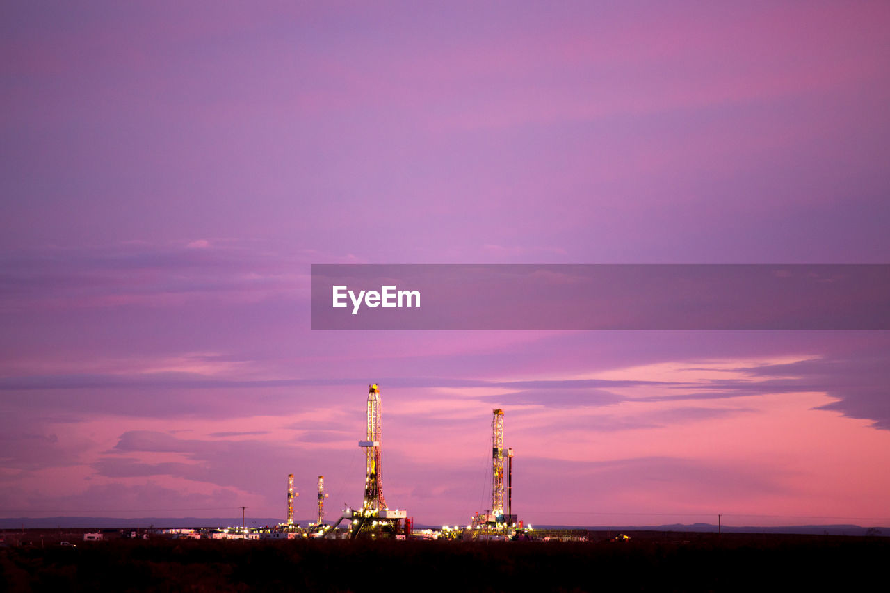 Drilling rig on field against cloudy sky